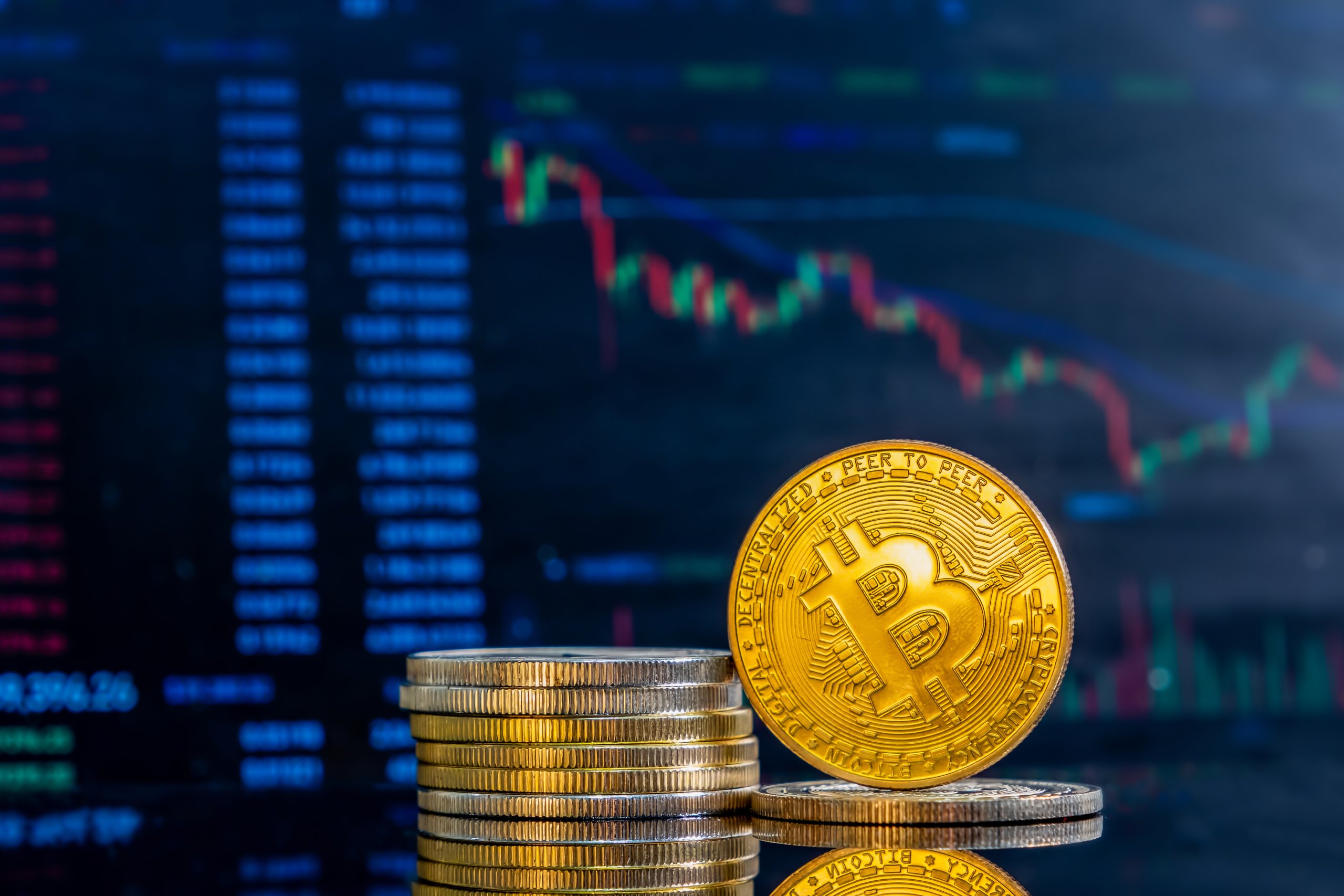 Close up of golden Bitcoins on a dark reflective surface and the histogram of decreasing crypto in the background